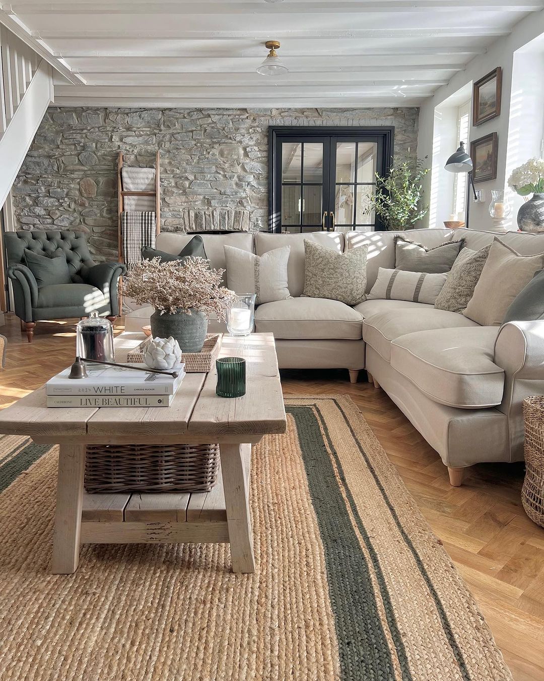 Beige sectional sofa with patterned cushions on a beige jute carpet in a rustic living room with stone walls and wooden coffee table.