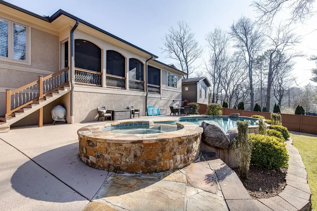 The exterior of a two story theo von's house featuring a stone hot tub and in ground swimming pool, a concrete patio, and a second floor screened in porch.
