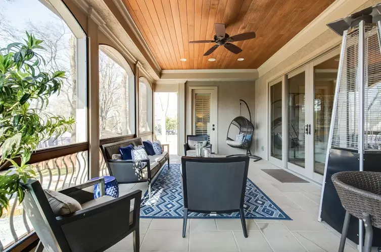 A modern screened-in porch with a wood plank ceiling, an outdoor ceiling fan, tile flooring, dark patio furniture, and glass doors leading into the house.