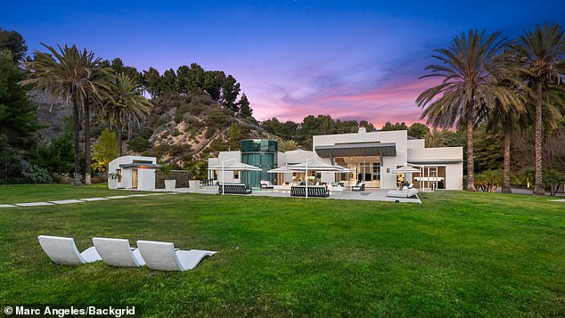 Luxury modern mansion with clean white architecture, expansive green lawn, outdoor lounge chairs, and palm trees under a colorful twilight sky