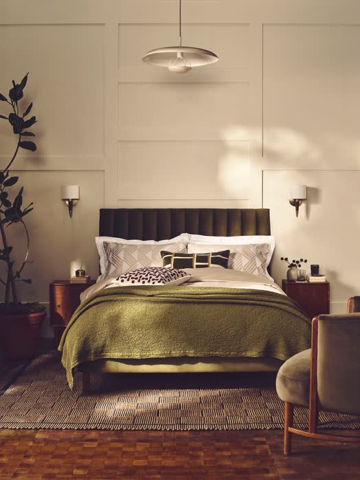 Dark moody green bedroom with dramatic lighting and rich layered textiles