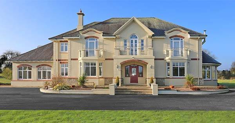 Exterior of Niall Horan's former Mullingar mansion showing the beige stucco two-story home with arched windows, red front door, and landscaped front yard in County Westmeath, Ireland