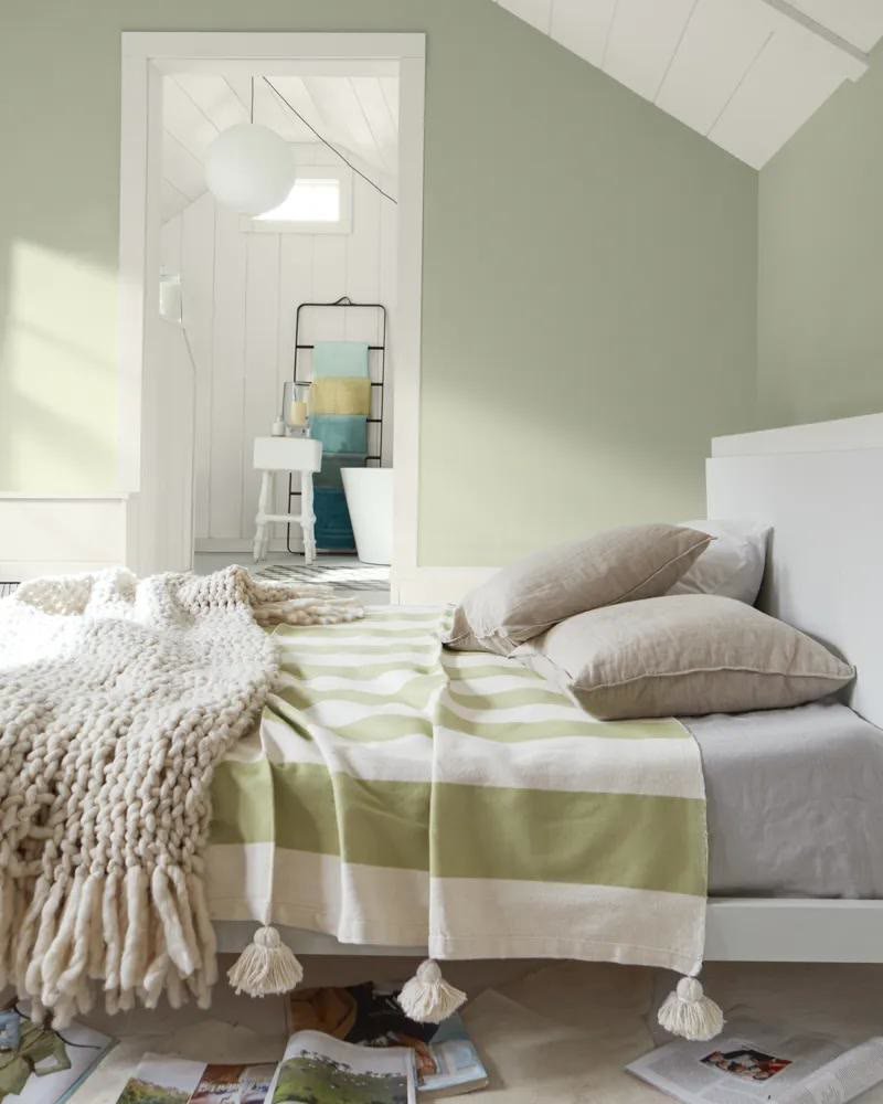Green and blue bedroom with navy cushions on a sage green bed and coastal artwork
