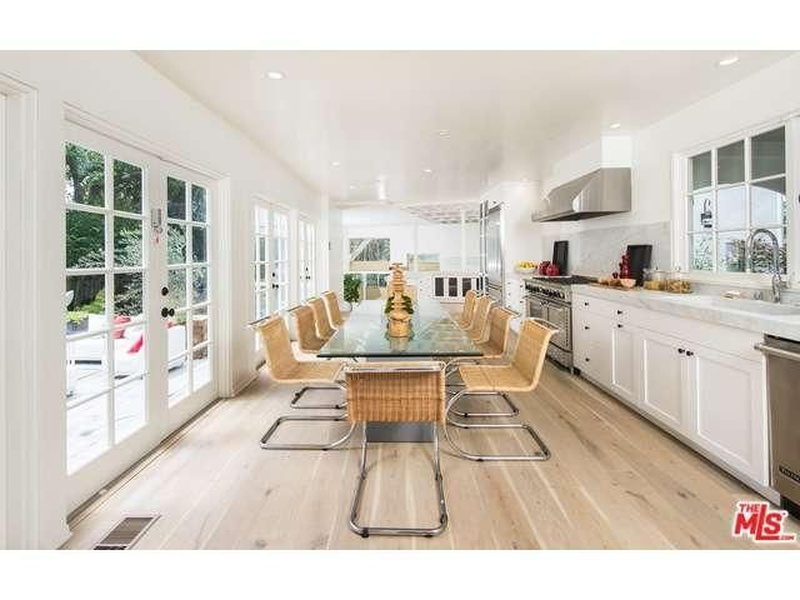 Kitchen and dining area of Niall Horan's Hollywood Hills home with white cabinetry, stainless steel appliances, glass-topped dining table, and French doors opening to the garden