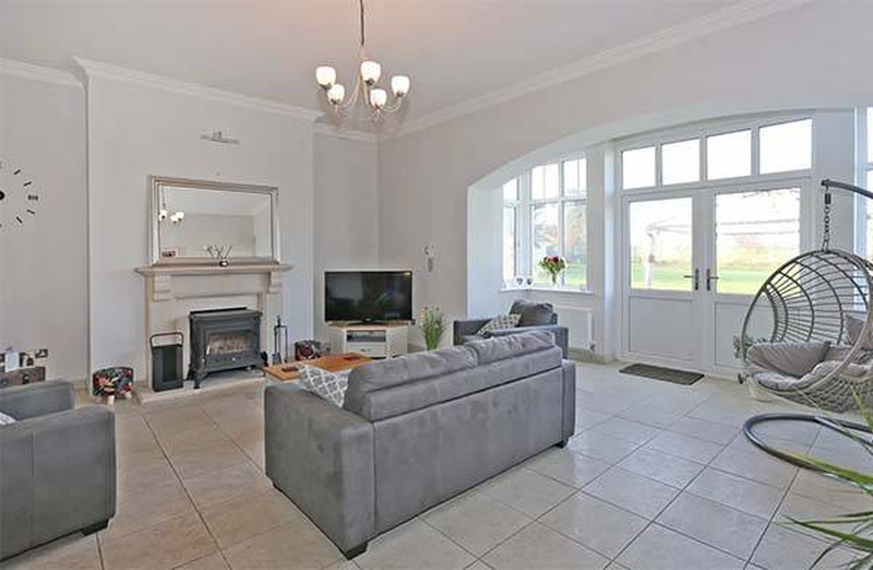 Living room inside Niall Horan's Mullingar mansion featuring a fireplace with mantel mirror, chandelier, arched windows, and views of the Irish countryside