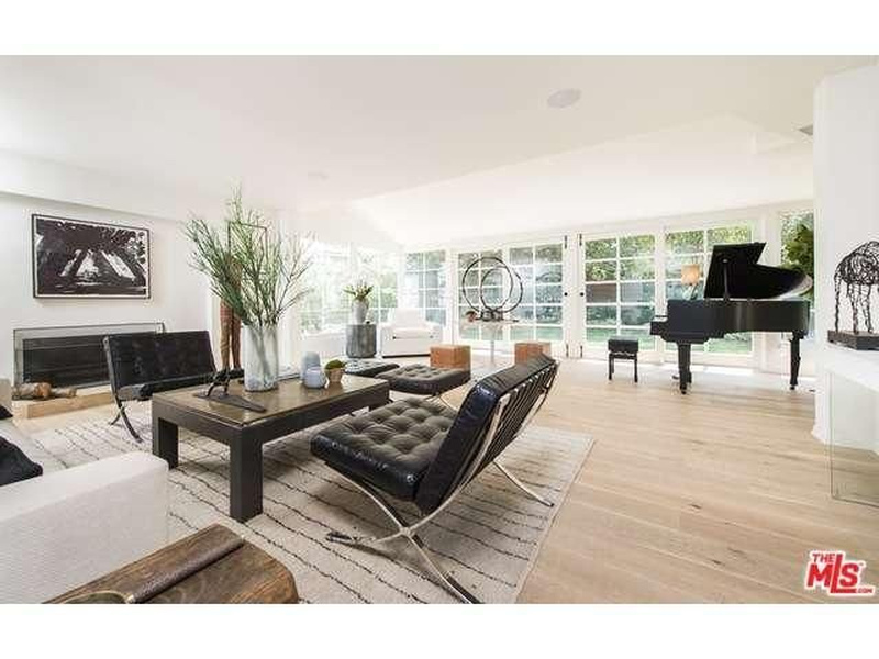 Living room of Niall Horan's Frank Gehry-renovated Hollywood Hills home featuring Barcelona chairs, a black grand piano, fireplace with abstract art, and large glass doors
