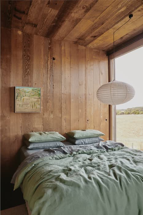 Moss green bedroom with rattan headboard, woven pendant light, and potted plants