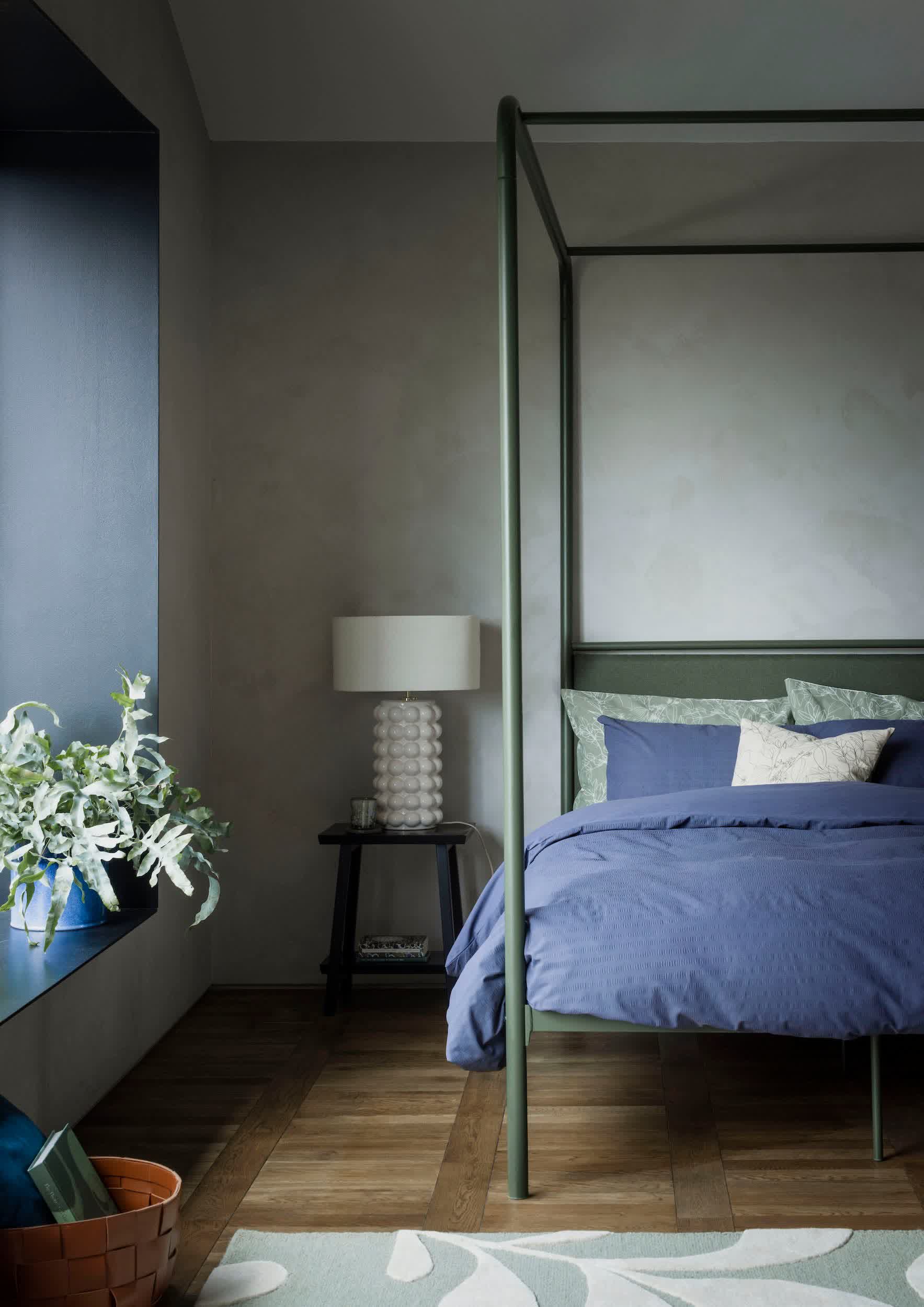 Soft green bedroom with layered linen bedding, a woven throw, and natural wood nightstand