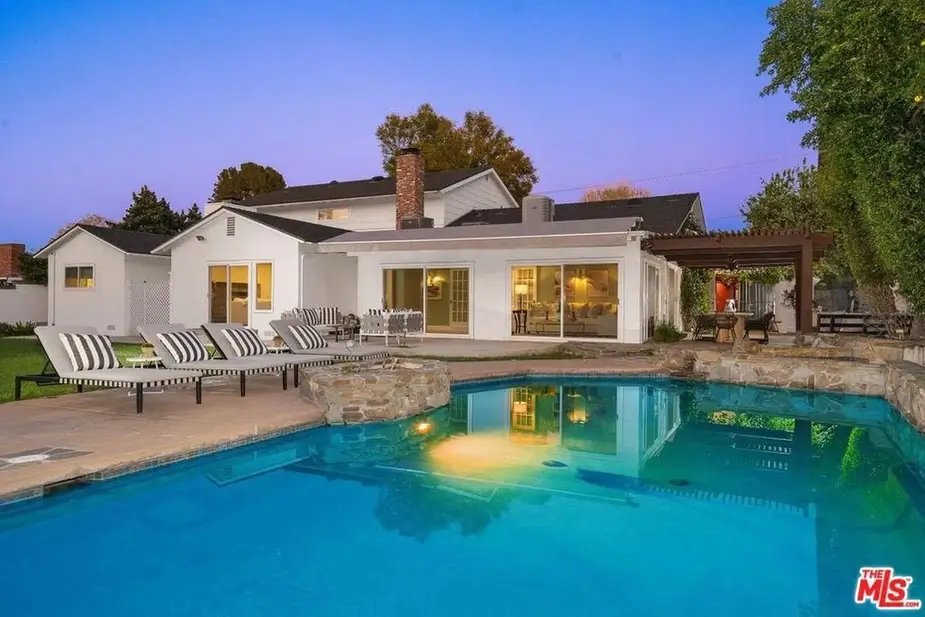 Tom Segura's Austin lakefront mansion pool area with patio, lounge chairs, and pergola at twilight.
